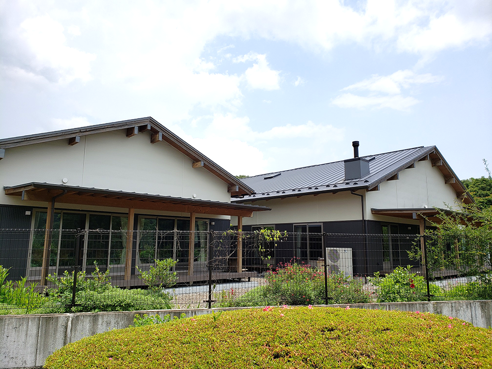 白と黒を基調とした現代的な介護施設の建物外観。広いウッドデッキと庭園が特徴。